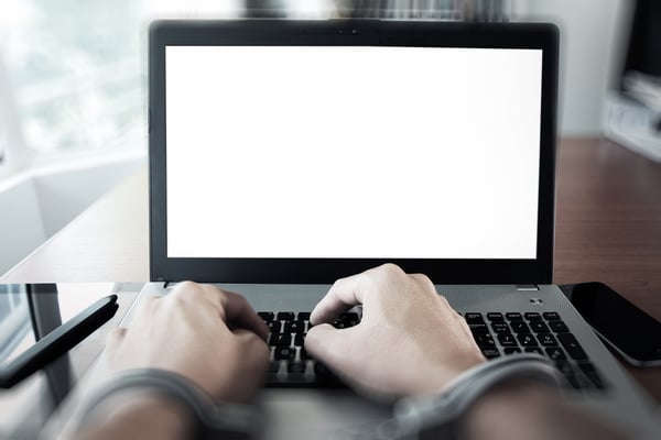 Businessman hand in handcuffs at wooden desk with laptop computer and digital tablet and stylus pen and smart phone as Cyber-Crime concept