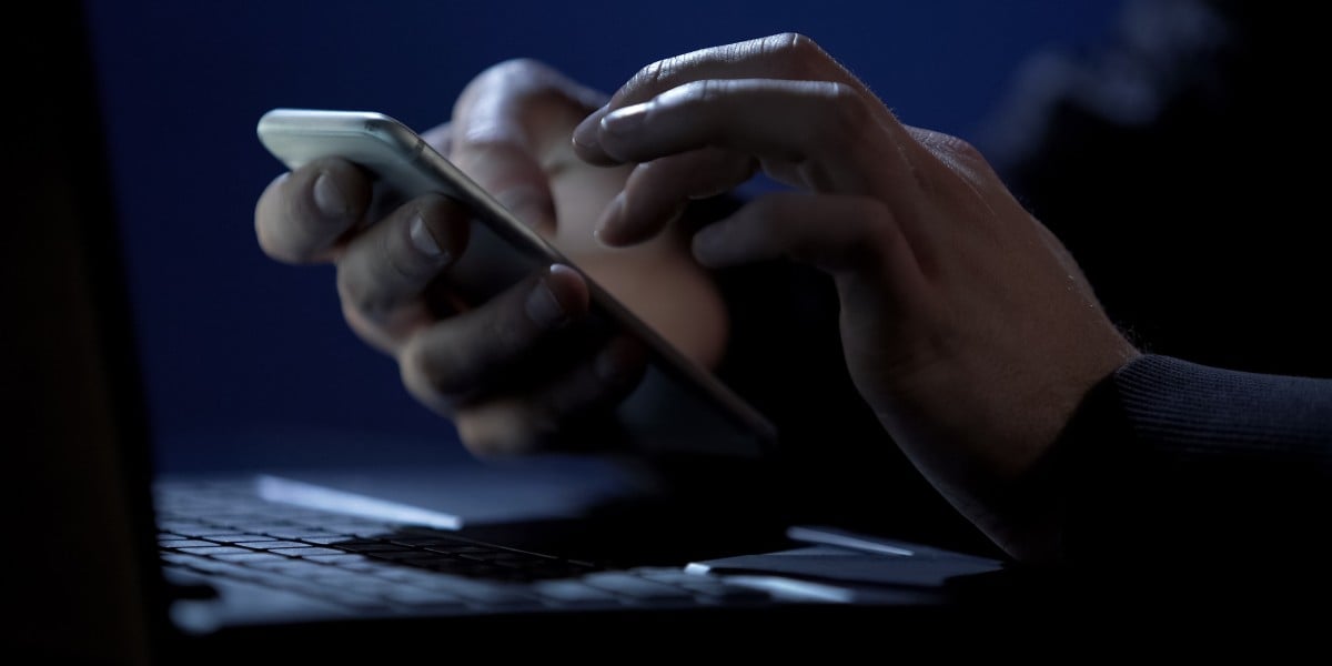Hands using smartphone while holding it above laptop keyboard
