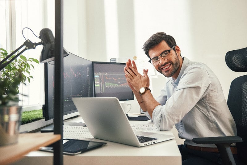 man sitting in front of monitors and a laptop smiling